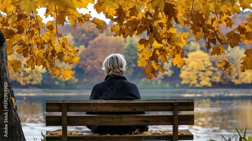 A person sits quietly on a bench by the river, surrounded by vibrant autumn leaves, enjoying a peaceful moment