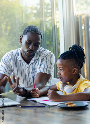 African American father helping son with homework at home, using laptop and notebook