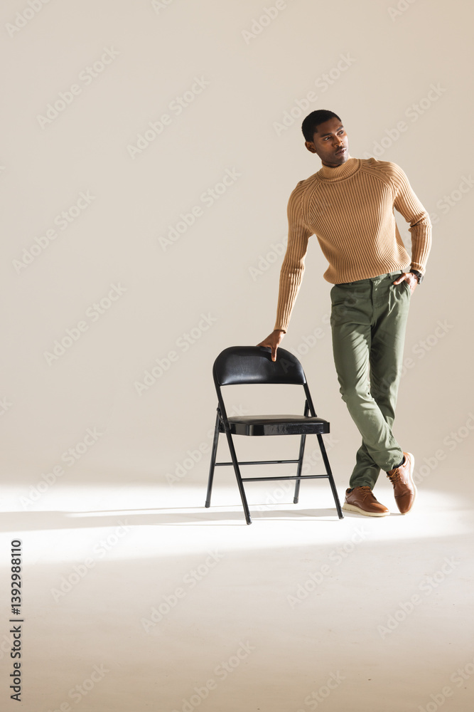 Stylish man in sweater leaning on chair, posing confidently in studio Stylish man in sweater leaning on chair, posing confidently in studio