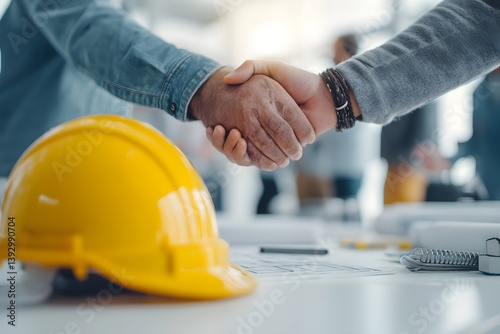 two construction workers shake hands in a business meeting, symbolizing partnership and teamwork. A yellow hard hat is on the table, symbolizing safety and professionalism