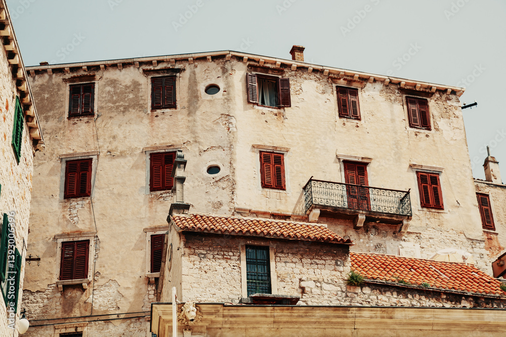 Rustic Mediterranean-style stone building with red shutters and tiled roof under clear sky Rustic Mediterranean-style stone building with red shutters and tiled roof under clear sky