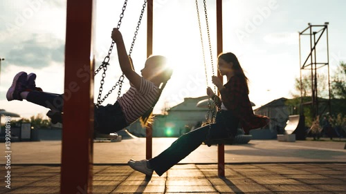 Happy female baby kid and adolescent swinging on swing at wooden sunny playground public park side view. Overjoyed girl children relaxing outdoor flying freedom leisure recreation activity bright sun