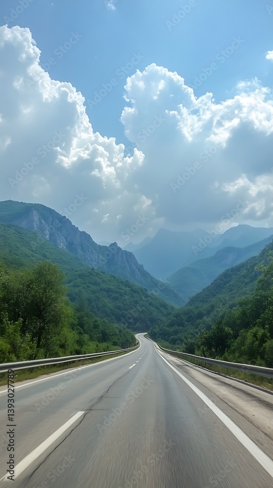 Fototapeta premium A scenic road winding through lush green mountain valleys under clouds