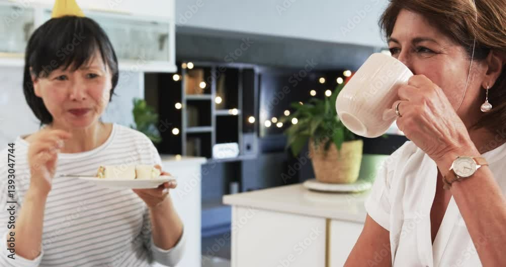 Happy senior diverse female friends eating cake and drinking coffee at birthday party in kitchen Happy senior diverse female friends eating cake and drinking coffee at birthday party in kitchen