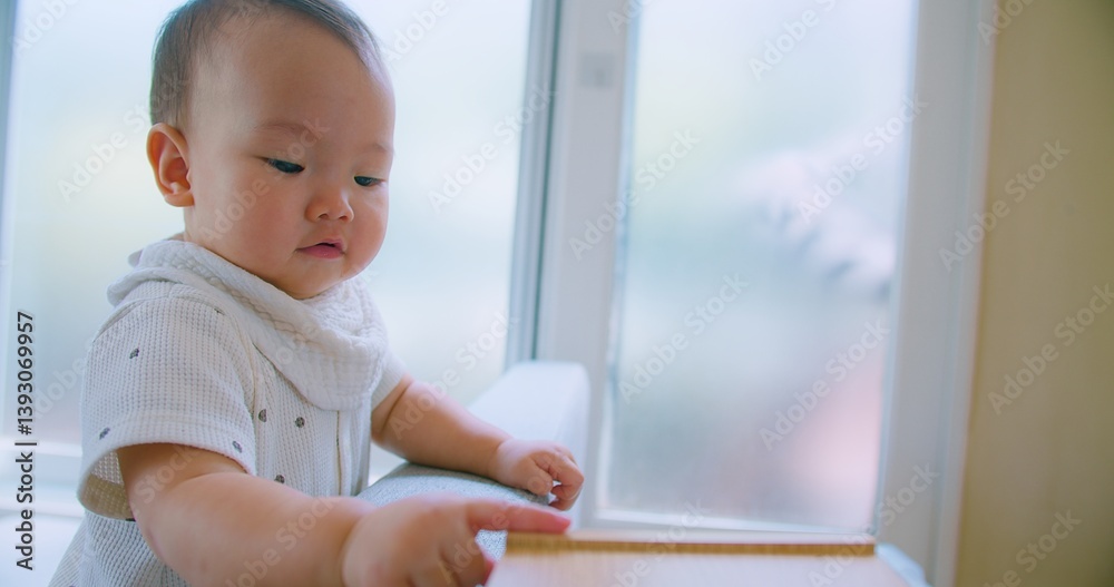 Curious Asian Baby Exploring Home Environment on Sofa in Bright Living Room with Natural Light with a curious expression. Curious Asian Baby Exploring Home Environment on Sofa in Bright Living Room with Natural Light with a curious expression.