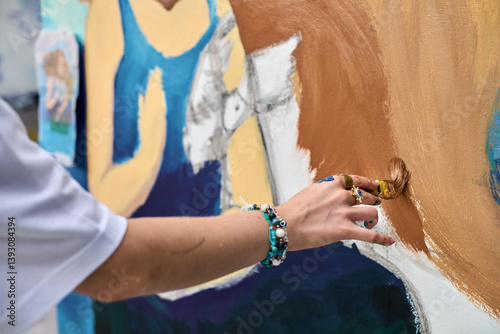 Female adult hand brings vibrant mural to life, showcasing creativity with brush strokes. Bright colors enrich outdoor canvas, blending art, nature, imagination