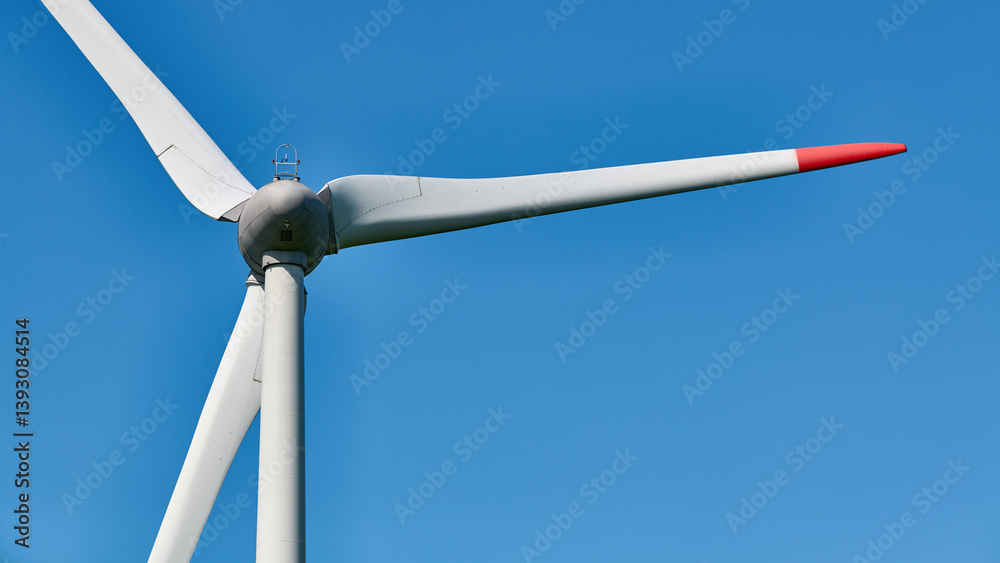 Detailed view of wind turbine with red tipped blades set against clear, vibrant blue sky on sunny day, evoking clarity and commitment to environmental sustainability Detailed view of wind turbine with red tipped blades set against clear, vibrant blue sky on sunny day, evoking clarity and commitment to environmental sustainability