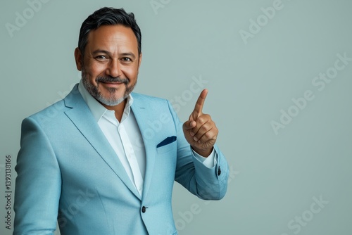 Man in Light Blue Suit Gestures With a Finger Pointing up Against a Neutral B...