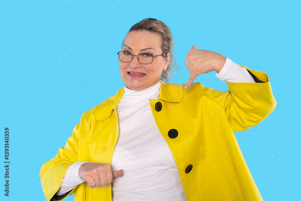 Woman in a bright yellow coat gestures call me playfully against solid blue background during cheerful photoshoot Woman in a bright yellow coat gestures call me playfully against solid blue background during cheerful photoshoot
