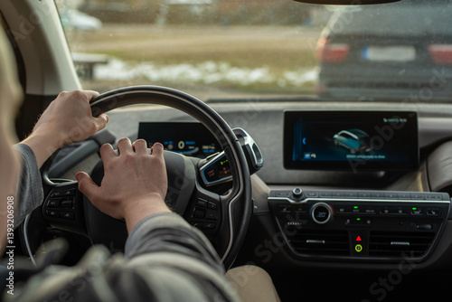 Close-up of a driver's hands pressing the horn while gripping the steering wheel of an electric car. Dashboard displays driving data. Urban road in the background. Road aggression, traffic jam concept