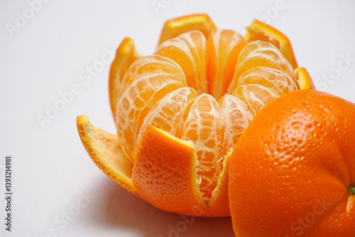 An unpeeled orange standing next to a segmented peeled orange, arranged symmetrically on a bright white background. Stock photography style.