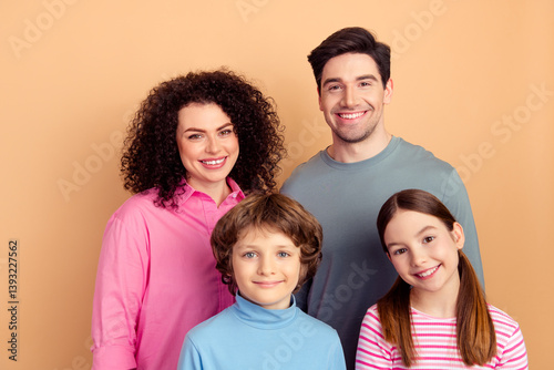 Cheerful young family posing together against a beige background, featuring two parents and their cheerful children