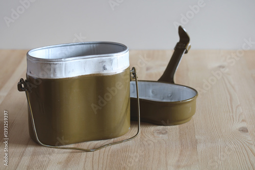 Military mess kit sitting on wooden table, showing cooking pot and pan