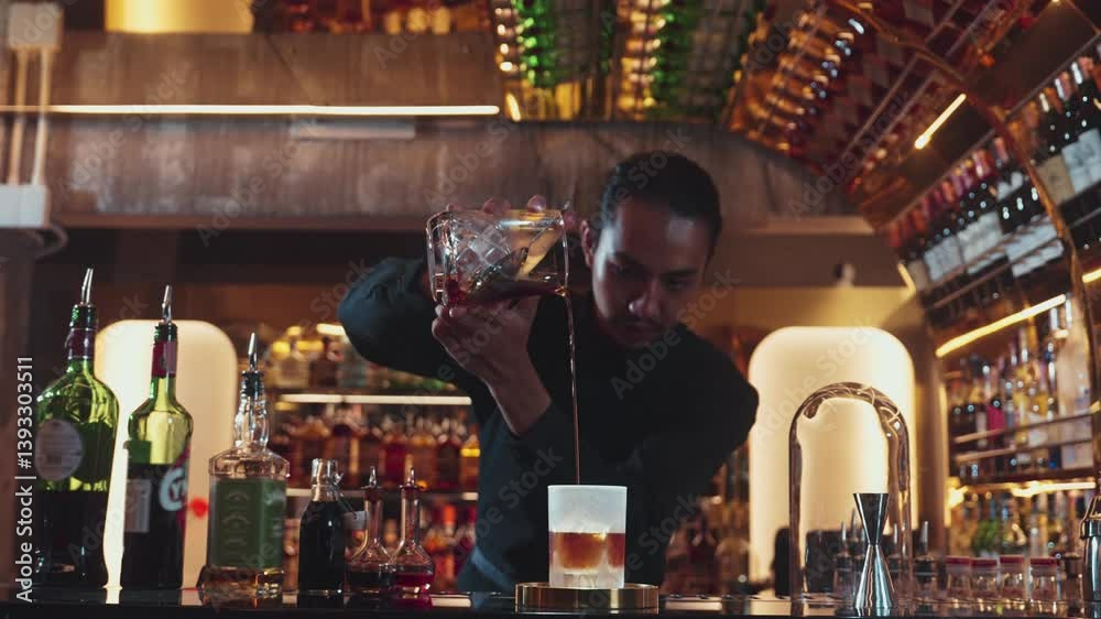 Asian bartender pouring mixed cocktail whiskey into cool glass textured cooling ice drink making special advertisement creative focusing alcohol refresh showcase at luxurious warm light pub. Vinosity.