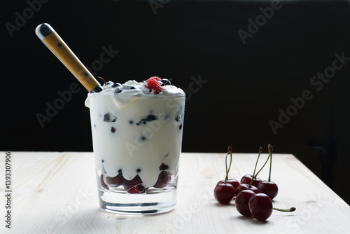 A glass of yogurt and fresh berries with a spoon on a wooden table. Side view
