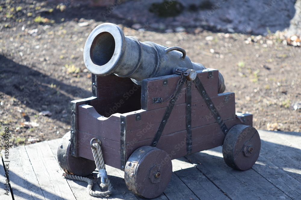 A historic-style cannon resting on top of a wooden cart, ideal for use in scenes depicting battles or military displays.