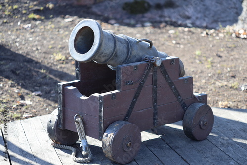 Obraz na płótnie A historic-style cannon resting on top of a wooden cart, ideal for use in scenes depicting battles or military displays. w salonie