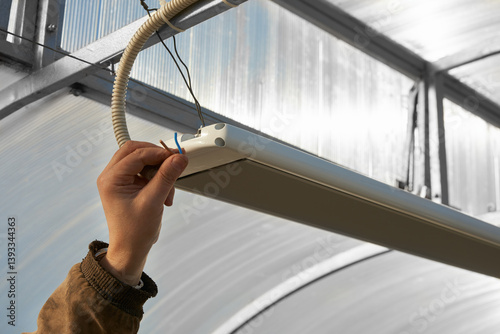 Obraz na płótnie Electrical wiring in a polycarbonate greenhouse to the infrared heater. A man's hand with a wire at the lamp. w salonie