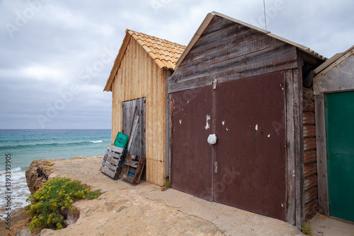 Rustic wooden barns set against a scenic ocean backdrop under a cloudy sky.