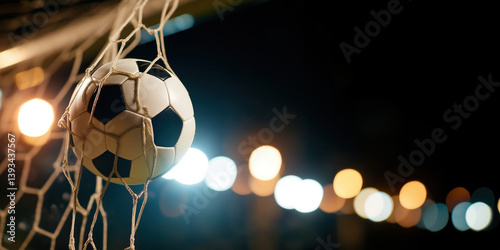 Obraz na płótnie A classic black and white soccer ball is caught in the white netting of a goal, with blurred stadium lights visible in the dark background. w salonie