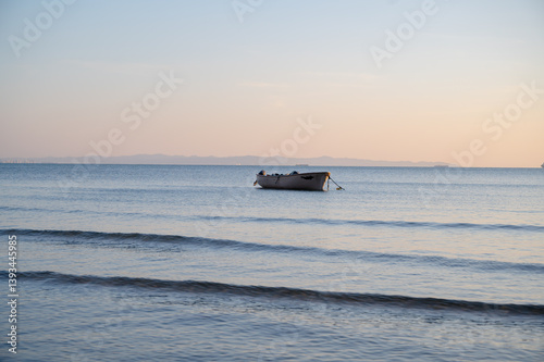 Obraz na płótnie A single boat floating quietly in the open sea under a clear sky. Minimalist seascape with calm water and a peaceful atmosphere. w salonie
