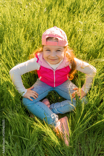 A cheerful girl sits in the thick green grass with her hands on her knees. Walk outdoors in the city park photo