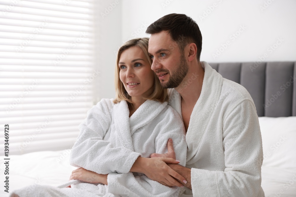 Spa. Happy couple in bathrobes sitting on bed indoors Spa. Happy couple in bathrobes sitting on bed indoors