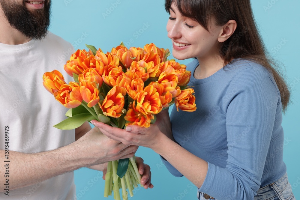 Man presenting bouquet of beautiful tulips to his beloved woman on light blue background, closeup