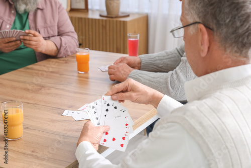 Elderly men with drinks playing cards at home, closeup