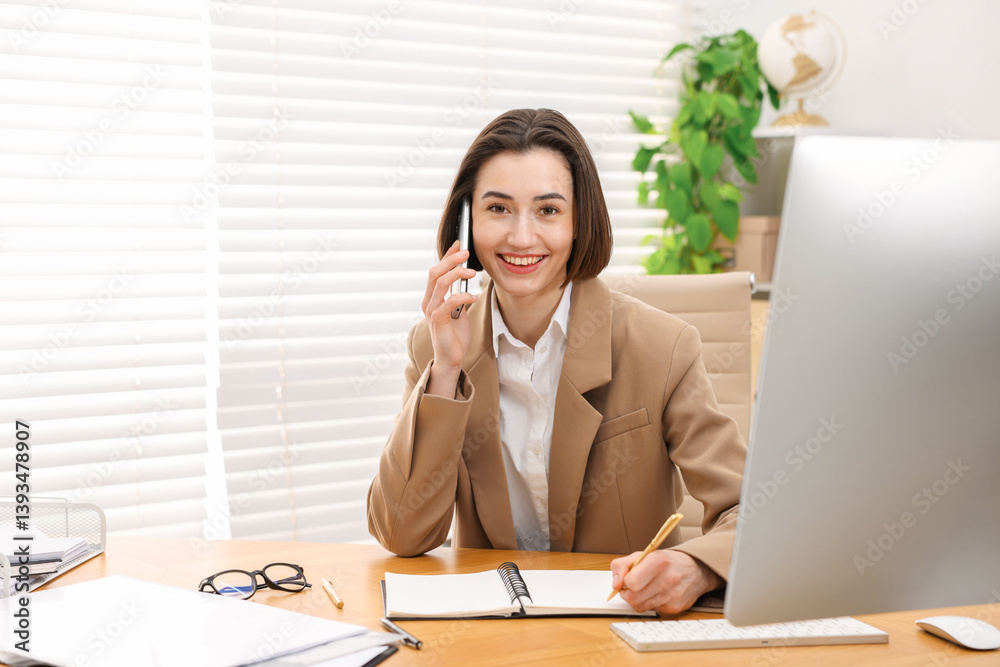 Smiling secretary talking on smartphone and taking notes at table in office Smiling secretary talking on smartphone and taking notes at table in office