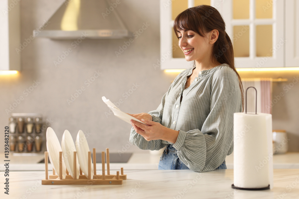 Woman wiping plate with paper towel at white marble table in kitchen