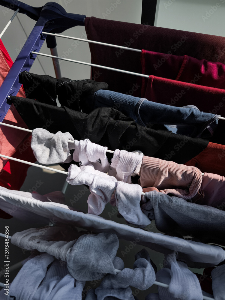 Freshly washed laundry hanging on a clothes rack, displaying a variety of everyday clothing items, including shirts and socks, in a tidy home setting