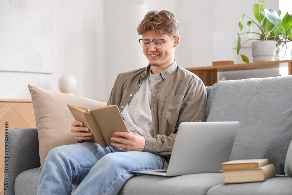Male student with book studying online on sofa at home Male student with book studying online on sofa at home