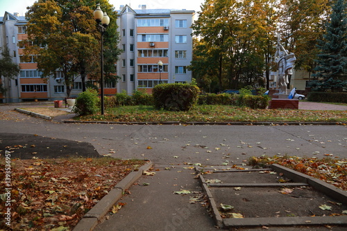 Fototapeta Naklejka Na Ścianę i Meble -  Beautuful old small town street view with house and old iron design lamp among orange yellow foliage under the blue autumn sky.