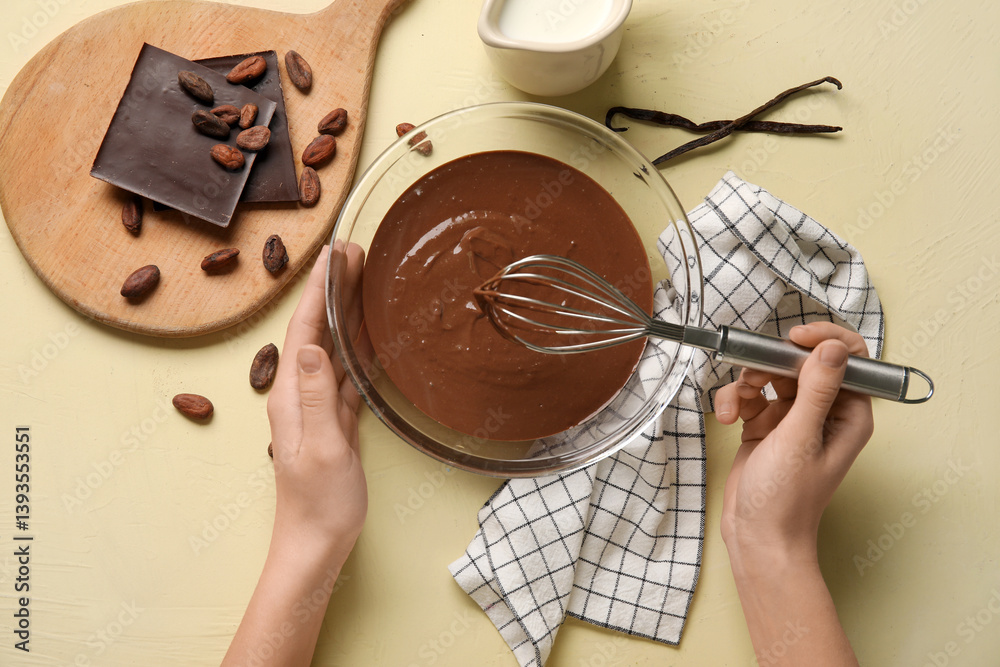 Female hands whisking melted chocolate on beige background. Top view