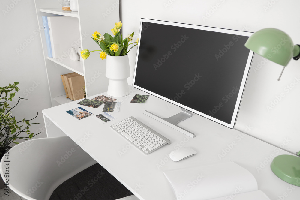 Obraz premium Vase with flowers and blank computer monitor on desk in light office