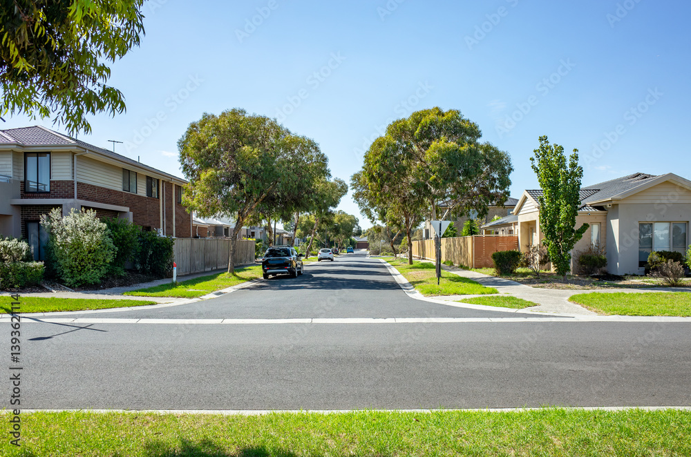 Fototapeta premium A quiet suburban street with modern houses and family homes in Melbourne, Australia.&nbsp;A peaceful and clean residential neighborhood with manicured lawns and mature trees lining the asphalt roadway.