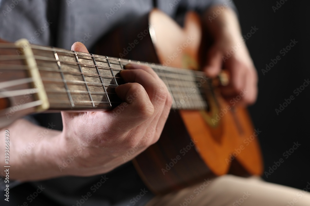 Obraz premium Man playing guitar on black background, focus on hand