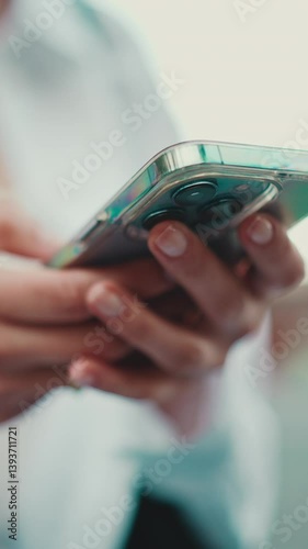 Vertical video, Closeup of young woman holds smartphone in her hands and scrolls through the news feed. Close-up of girl hand uses mobile phone outdoors in urban background
