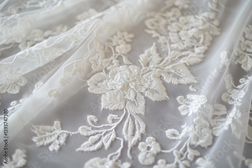 Delicate white Tambour lace fabric featuring intricate floral embroidery. The lace has a soft, sheer quality, showcasing detailed patterns of flowers and leaves.