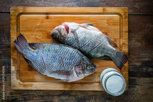 Fresh tilapia fish prepared for cooking with salt on wooden board