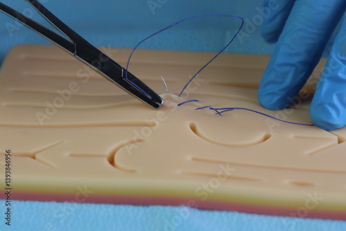 Healthcare professional wearing gloves training surgical suture with a needle in a wound simulation set. Close up in the surgical needle