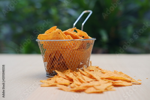 The image shows a small wire mesh basket filled with crispy, triangular corn chips, commonly known as nachos or tortilla chips