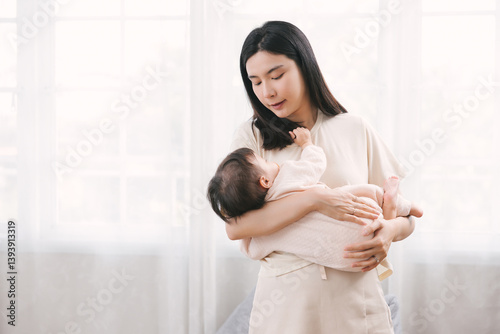 Asian mother gently holding and soothing her infant to sleep in bright, peaceful home setting. Natural, tender moment of maternal care and bonding. Parenting Moments, Heartwarming Family Lifestyle.