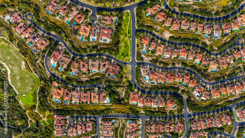 High-resolution aerial photograph showing a planned neighborhood with curved streets and luxury homes with red tile roofs and backyard swimming pools in Newport Beach, California. The community is sur