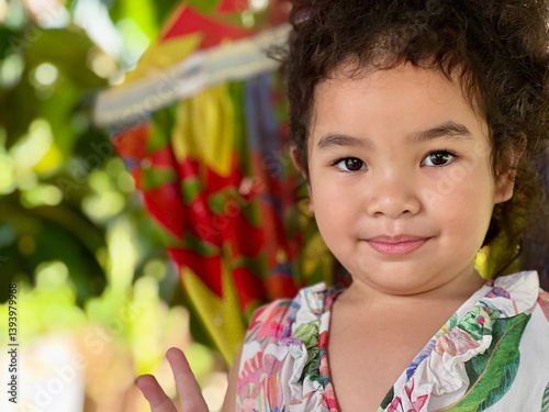 Portrait of a beautiful little Asian girl with curly hair in a garden