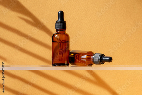 Two Unbranded bottles with pipette on glass shelf. Transparent container made of amber glass with oil for body and hair. Display sample on on a brown background in the sunlight. Mockup style design.