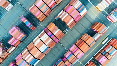 Aerial top view of organized stacks of colorful shipping containers at a busy cargo yard. The image reflects the logistics efficiency and volume of global trade through maritime transport.