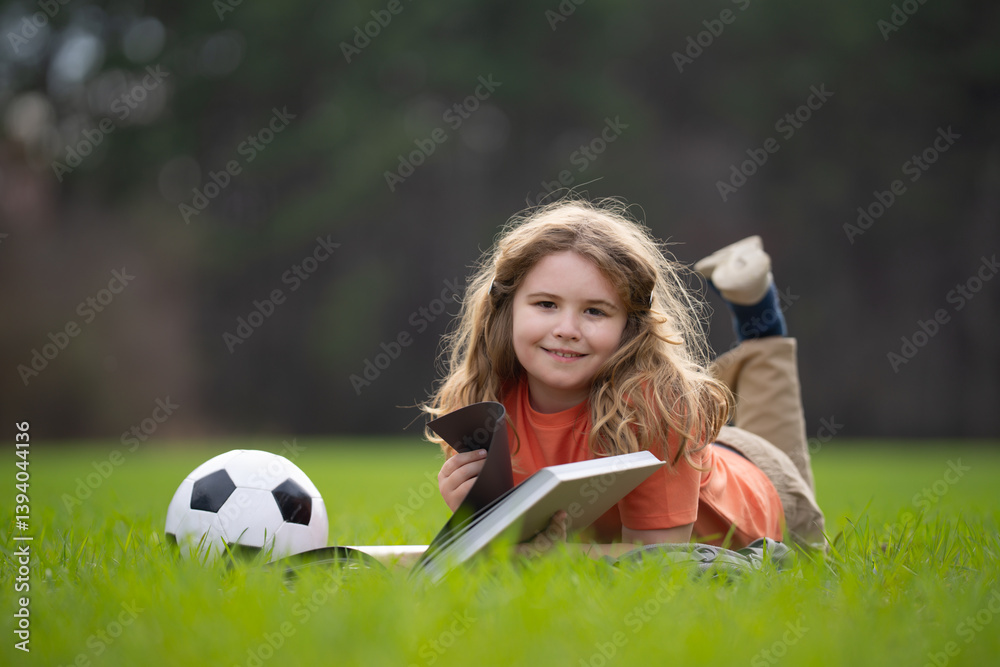 Fototapeta premium Kid read a book in the grass. Kid read a book story outdoors. Kid read book in the meadow on a sunny day. Reading in nature. Schoolboy with book. Kid outdoor learning. Kids read story.