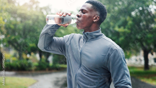 Obraz na płótnie Drinking water, outdoor and black man with fitness, healthy guy and exercise with thirsty. African person, athlete and runner in street, bottle and liquid with wellness, hydration and sports in park w salonie
